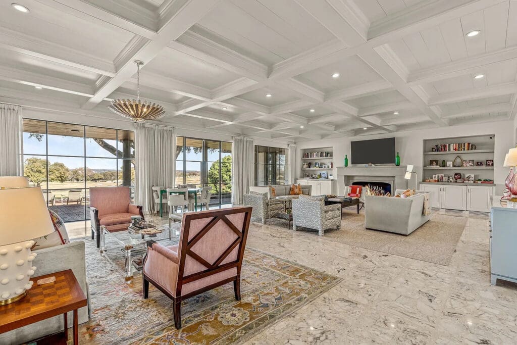 The grand living area boasts coffered ceilings, a gas fireplace, and panoramic golf course views. (Courtesy)