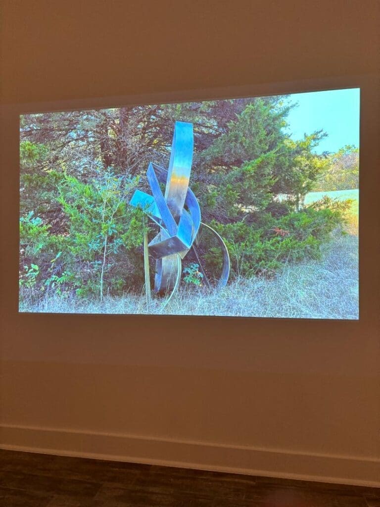 An installation view of "Mac Whitney: Interconnected Elements" at the Andrew Durham Gallery in Houston, December 7, 2024-January 25, 2025. Gallerist Andrew Durham filmed late artist Mac Whitney's studio and outdoor sculptures while visiting Whitney's land in Ovilla, Texas. (Photo by Ericka Schiche)