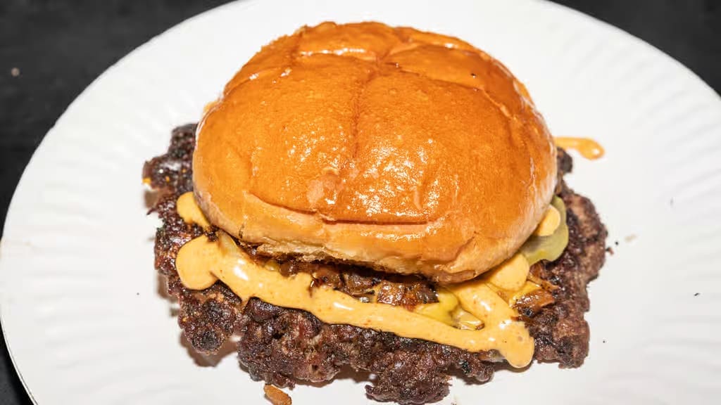 At GUSTOS Burger Bar + More, the house burger keeps it simple with juicy patties, grilled onions, pickles, and signature Gustos sauce on a toasted bun. (Courtesy)