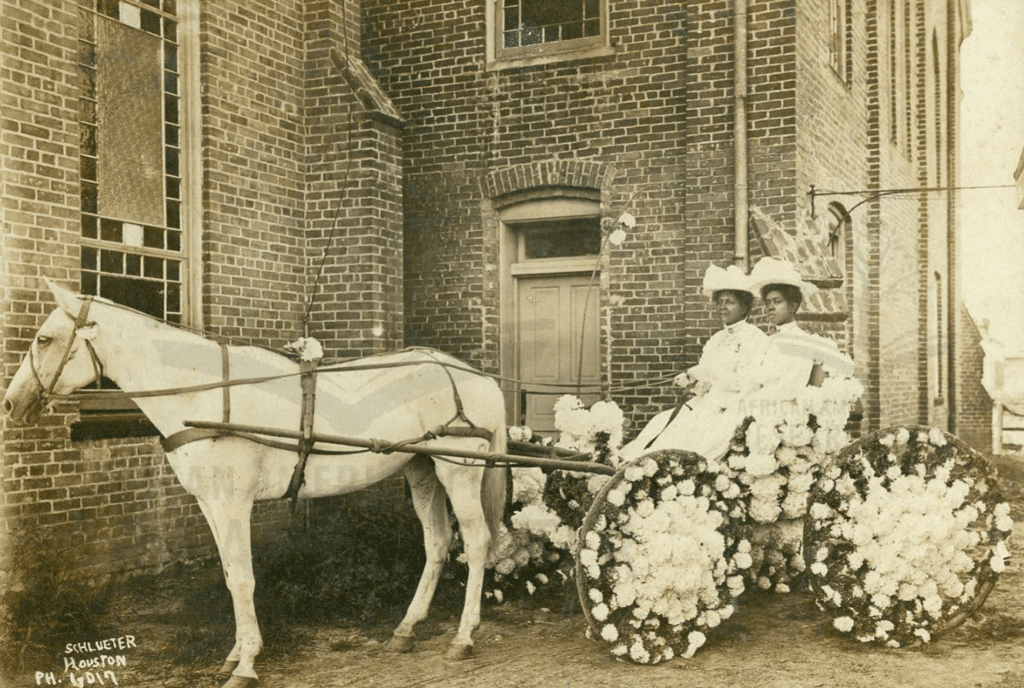 Martha Yates Jones and Pinkie Yates (both in white dresses and hats) sitting in a buggy decorated with flowers for the annual Juneteenth Celebration parked in front of Antioch Baptist Church located in Houston's Fourth Ward, Circa 1908. (Photo by Schlueters Advertising and Souvenir Photographs, Houston. Courtesy Community Artists' Collective and Houston Public Library)