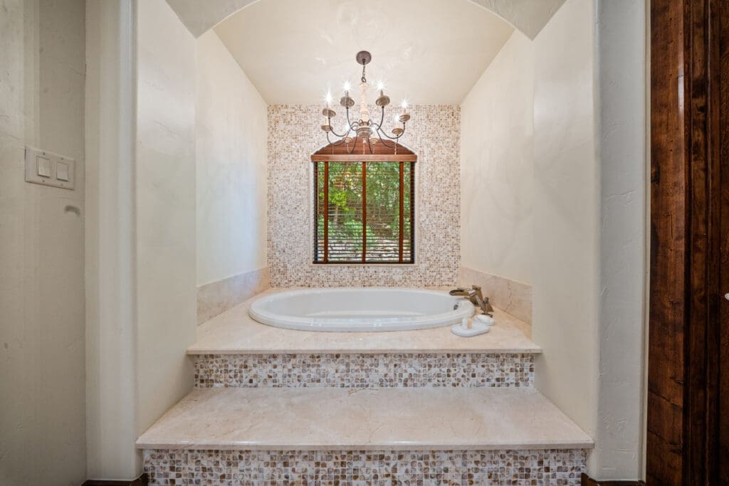 The primary suite’s spa-inspired bathroom features a soaking tub, mosaic tile, and views of the surrounding greenery. (Photo by The Ashton Agency)