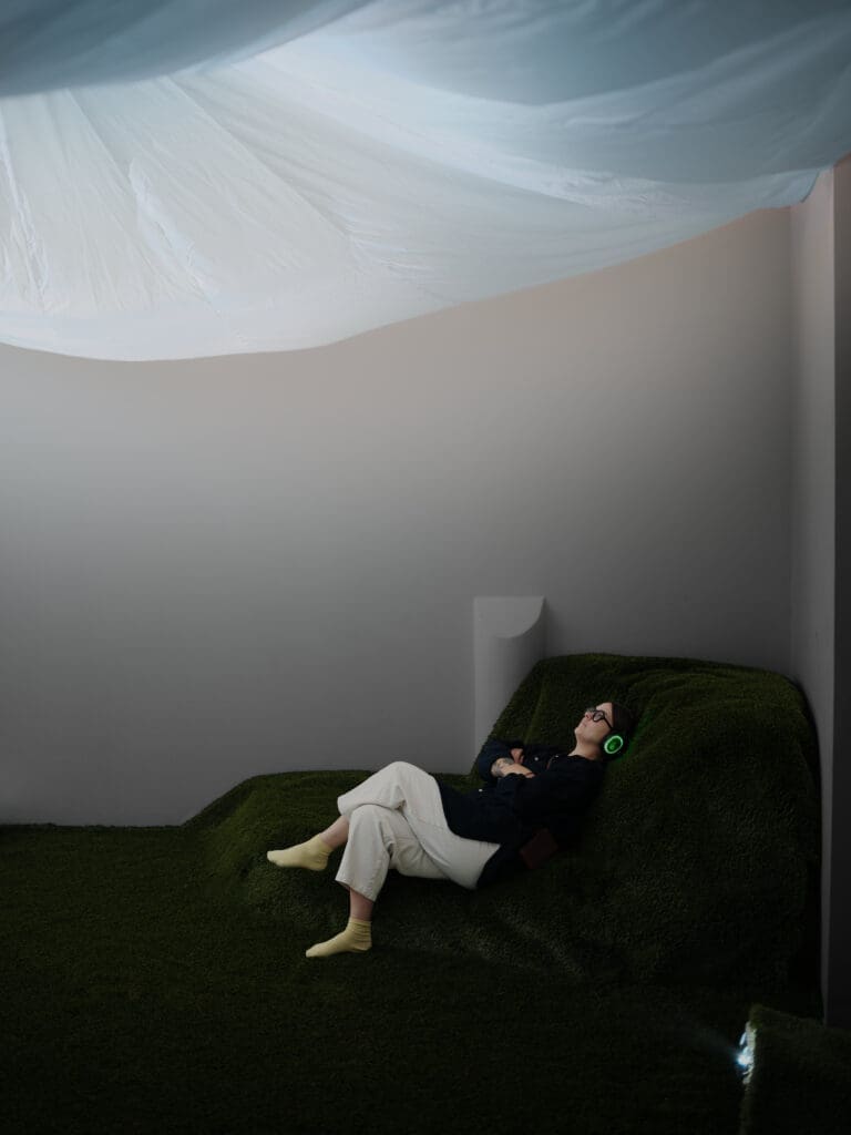Touch Grass encourages visitors to put their phones away, remove their shoes, lie back, and ground themselves in the space while observing the projection of the sky that washes across the ceiling.  (Photo by SWOON, the studio)