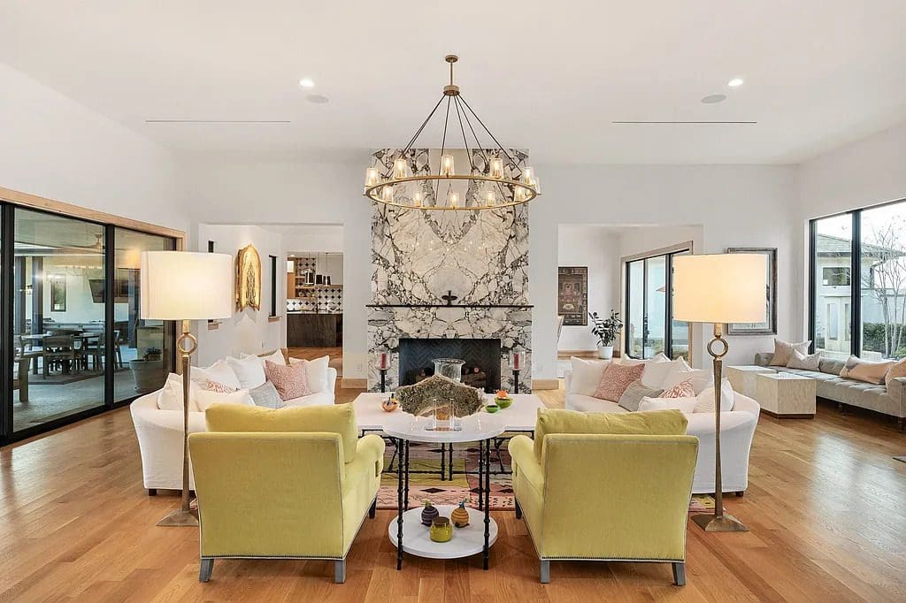 A marble-clad fireplace anchors the main living room, where expansive windows frame views of the surrounding property. (Courtesy)