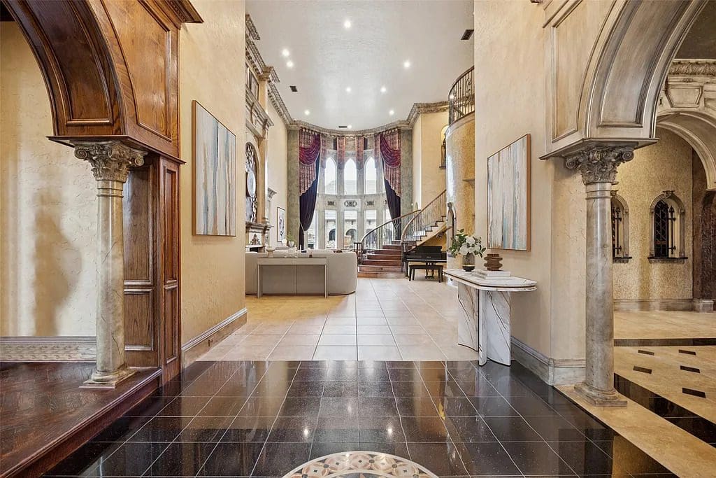 A dramatic entryway welcomes guests with marble columns, soaring ceilings, and a sweeping staircase leading into the main salon. (Courtesy)