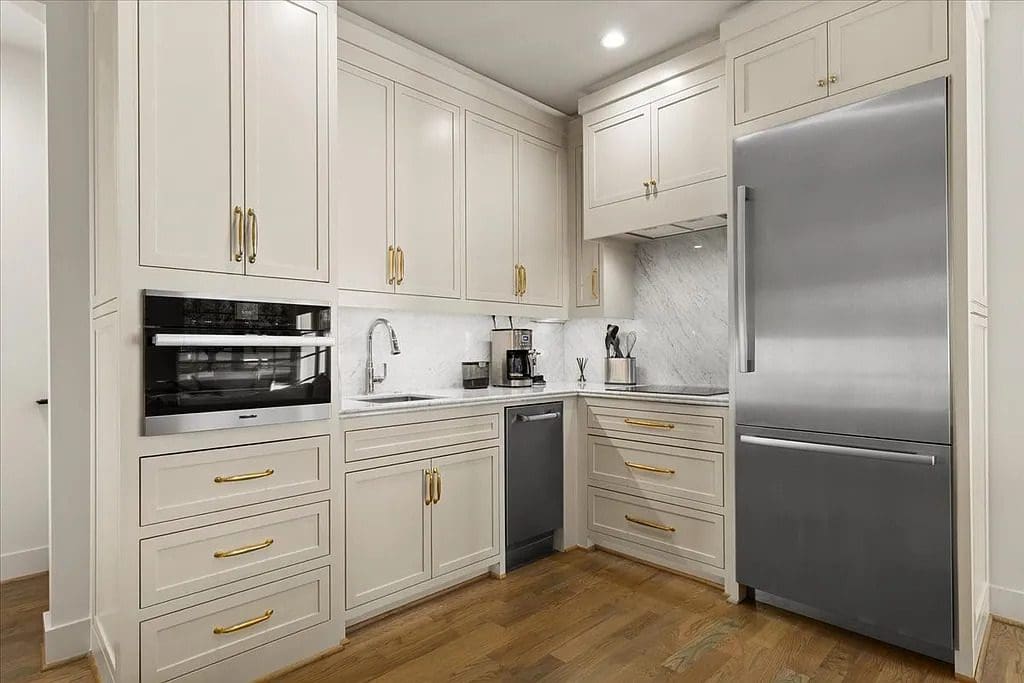 The kitchen blends classic cabinetry with modern appliances and brass hardware, offering a clean, functional workspace. (Courtesy)