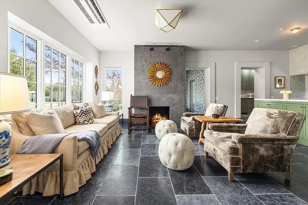 A central living space combines stone flooring, layered seating, and a modern fireplace, creating a relaxed yet refined gathering area. (Courtesy)