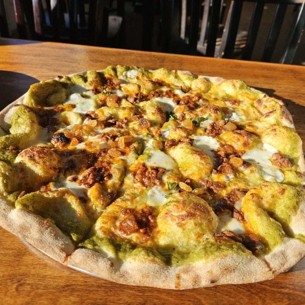 The La Felina pizza comes on a thin, crispy dough that as topped with mozzarella, dollops of a rich, meaty ragu, a poblano crema, and golden raisins. (Courtesy)