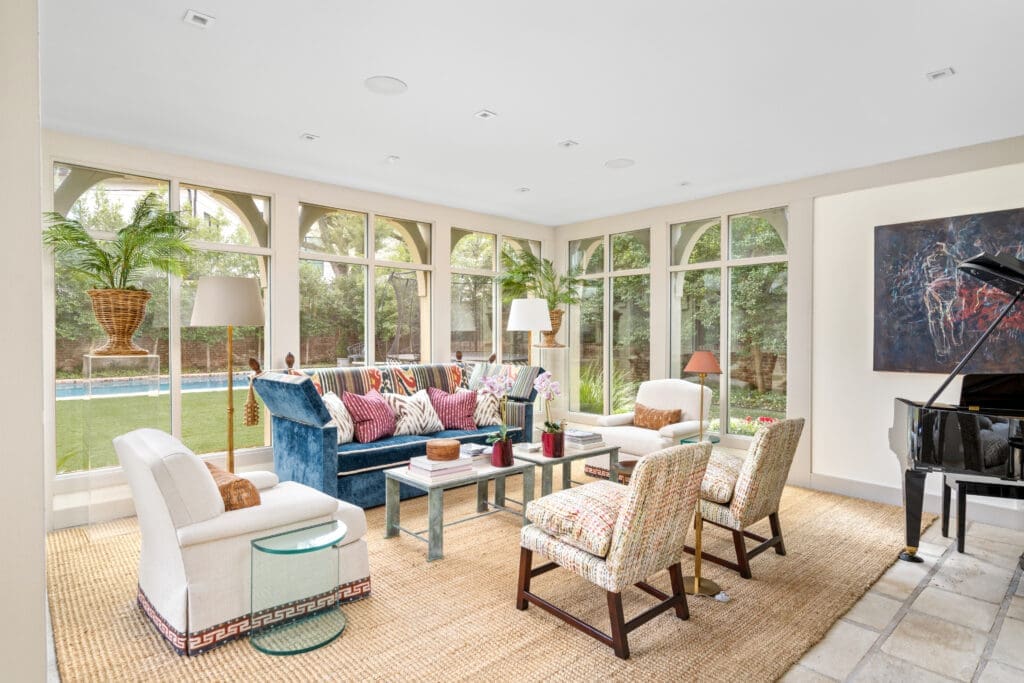 Light-filled sunroom framed by expansive windows, offering views to the terrace and pool beyond (Photo by Sonya Bertolino / Compass)