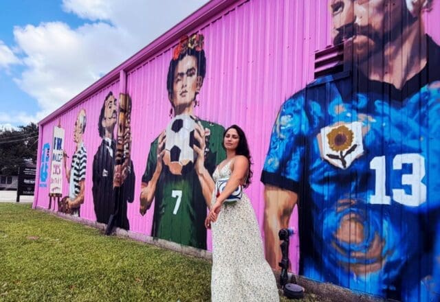 Artist and muralist Jatziri Barron stands near her mural, "The Art of the Beautiful Game," 2026, which features artists Pablo Picasso, Salvador Dalí, Frida Kahlo and Vincent Van Gogh. (Courtesy Jatziri Barron)