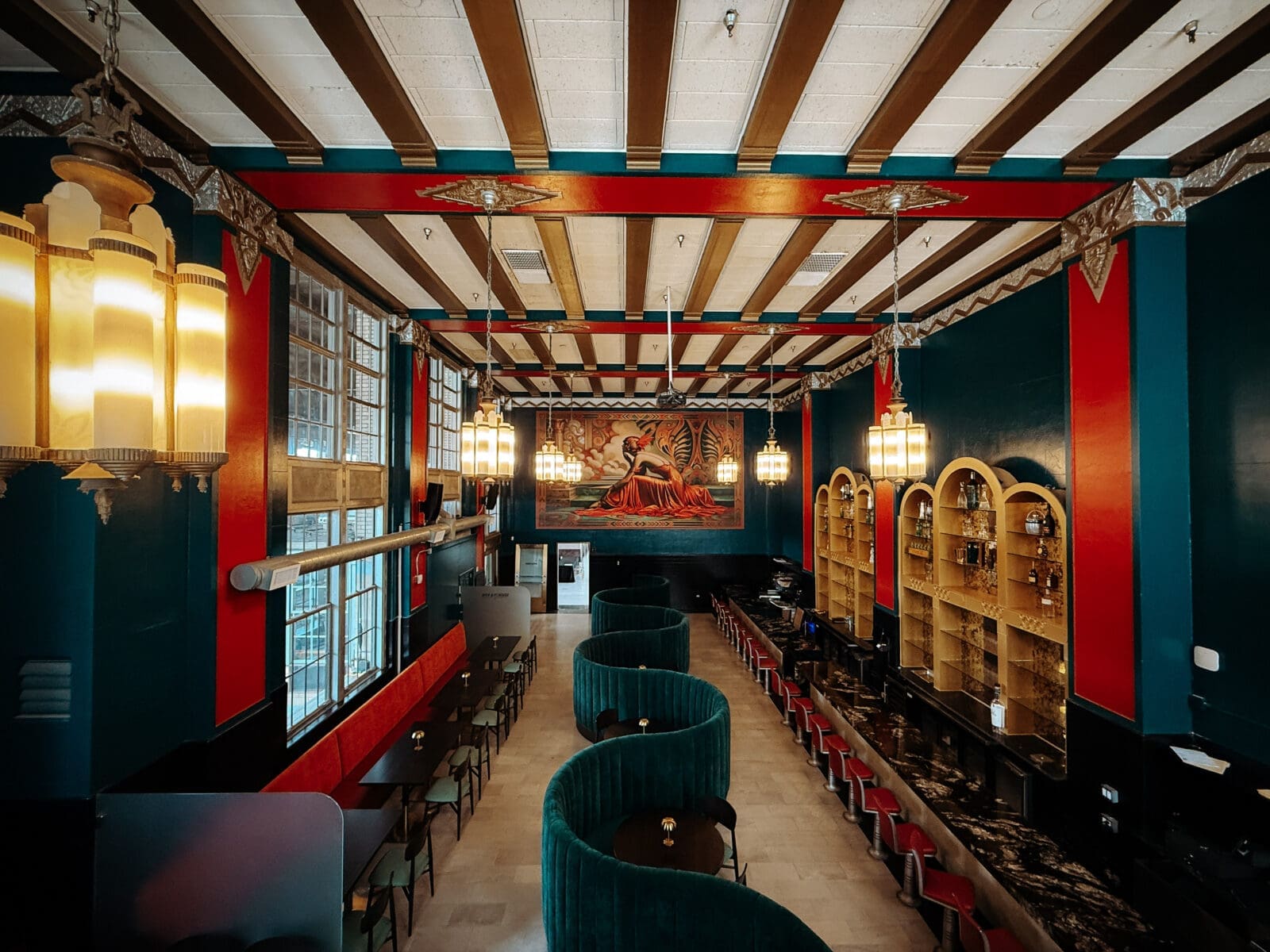 Deep teal velvet banquettes and a dramatic ruby-red mural give the dining room a lavish, almost fantastical Art Deco aesthetic. (Photo by Chancee Proctor and Teshorn Jackson )